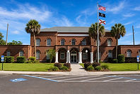 A front view of the Gilchrist County Courthouse in Florida, featuring its red brick facade and white-arched portico, serving as the site for probate and estate proceedings