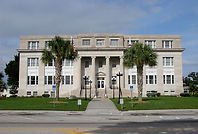 Exterior view of the Highlands County Courthouse in Sebring, Florida, a stately two-story building with columns that houses the Highlands County Probate Court, with the entrance flanked by palm trees and American flags