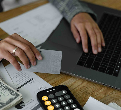 Persona revisando facturas y documentos financieros mientras sostiene una tarjeta de pago frente a una computadora portátil, representando las reclamaciones de acreedores, las deudas pendientes y las obligaciones financieras en un caso de sucesión en Florida