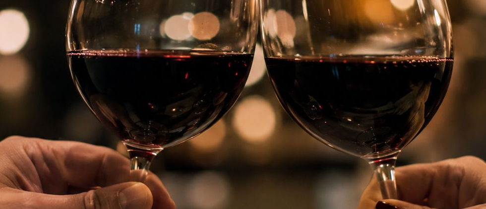Two people toasting glasses of red wine at a Wine and Wills estate planning event with warm ambient lighting