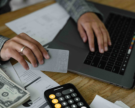 Person reviewing bills and financial documents while holding a payment card at a laptop, representing creditor claims, outstanding debts, and financial obligations in a Florida probate case