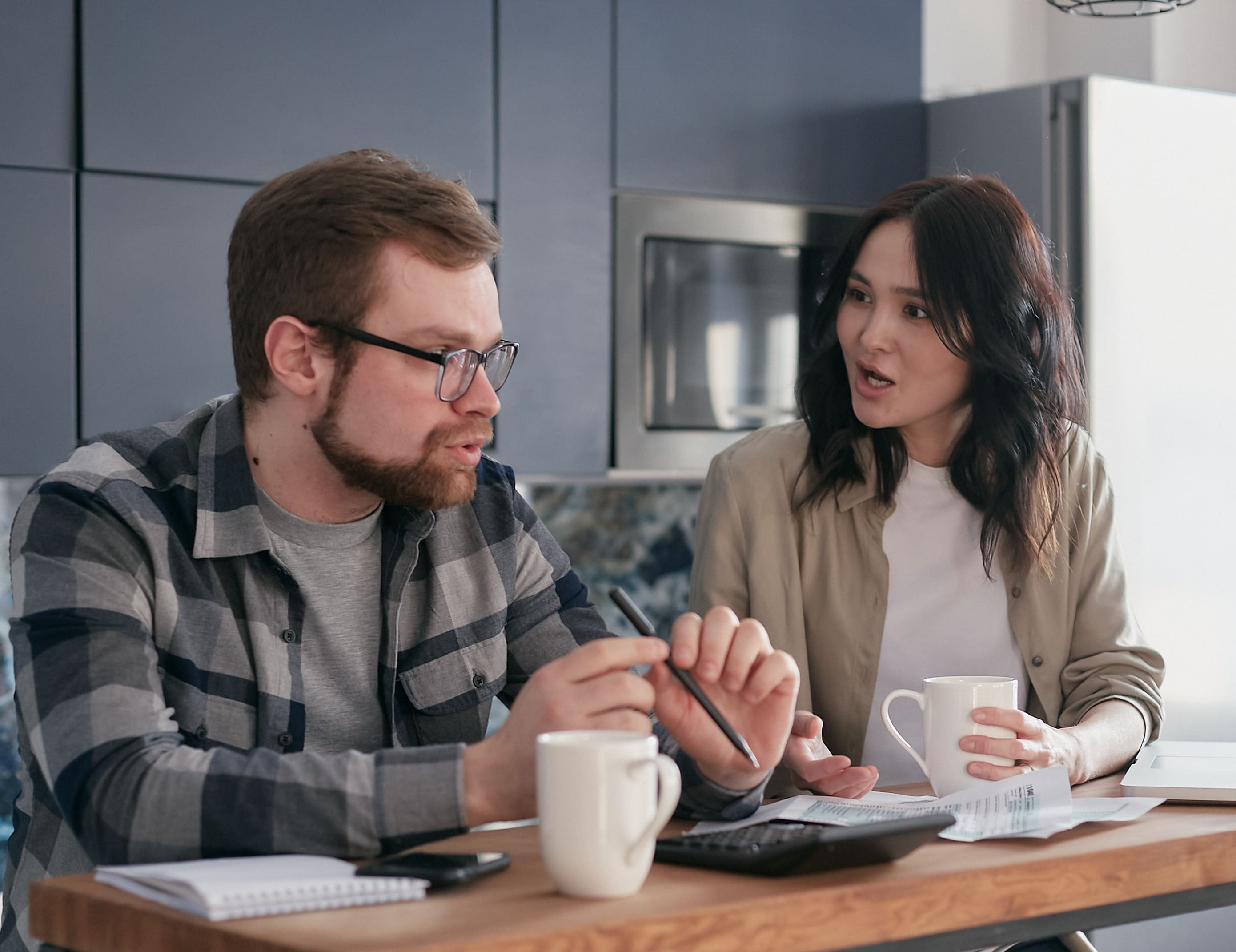 Married couple discussing finances and estate planning decisions at their kitchen table, illustrating challenges when one spouse is reluctant to plan.