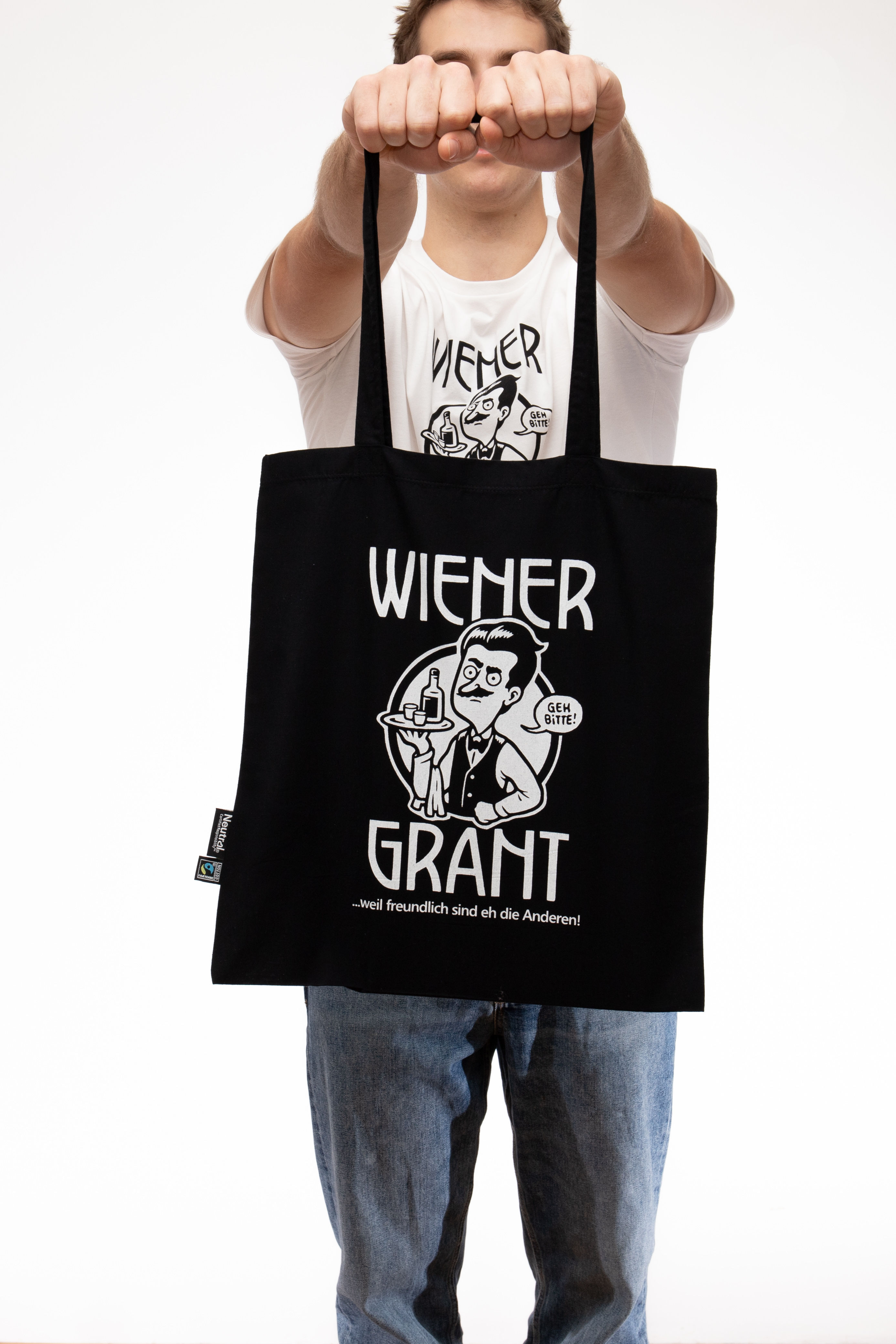 Person hält schwarze Tragetasche mit „Wiener Grant“ Aufdruck. 2x Wiener Grant Buttons DM 2,5cm.