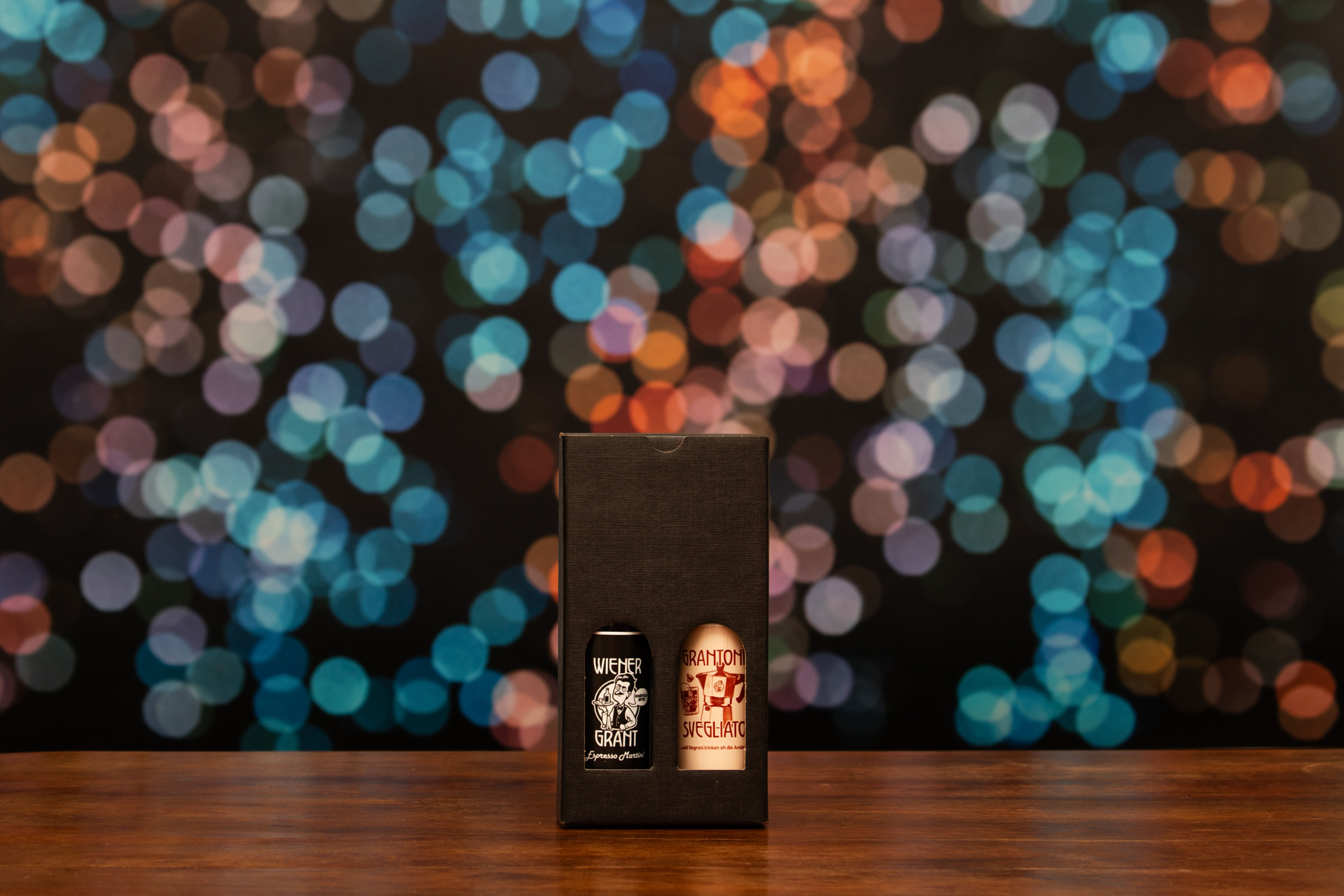 Zwei Flaschen in einer schwarzen Box, mit 2x Wiener Grant Buttons DM 2,5cm. Buntes Bokeh im Hintergrund.