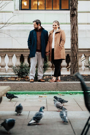 a couple standing in front of a group of particularly fat pigeons