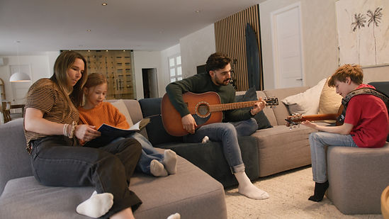 Un père et son fils jouent de la guitare, mère et fille lisent.
