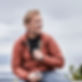 Homme souriant en doudoune orange regardant au loin, tenant un smartphone.