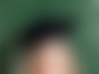 A woman in a black grad cap looking up, behind a green chalkboard with question marks written on it.