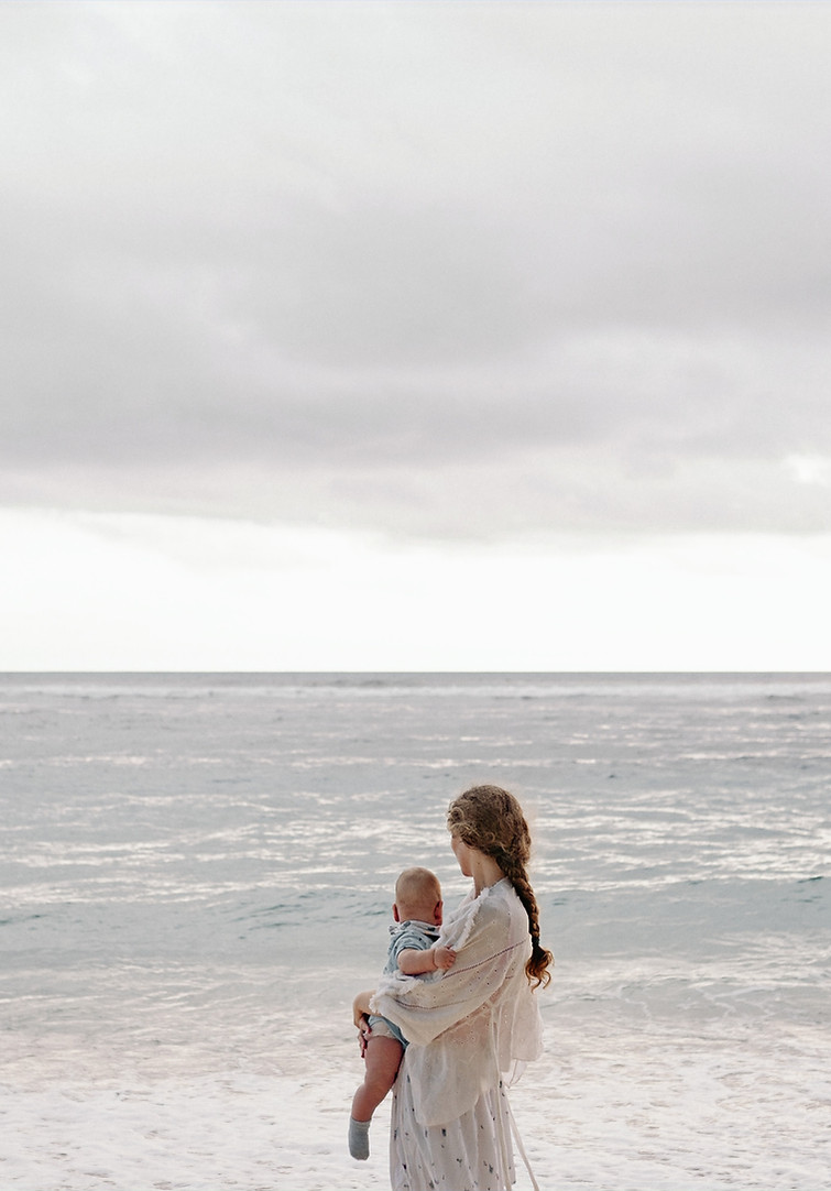 Sehnsuchtskind. Frau hält ein Baby im Arm und blickt auf das Meer. Symbol der Hoffung und Sehnsucht.jpg