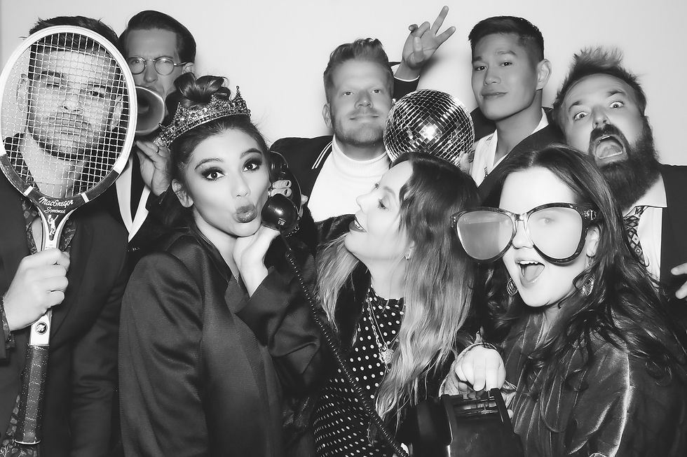 Group of joyful people posing with props like a tennis racket and crown in a fun setting. Black and white image, playful atmosphere.