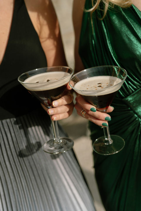 Close-up of guests holding espresso martini cocktails at a wedding reception.