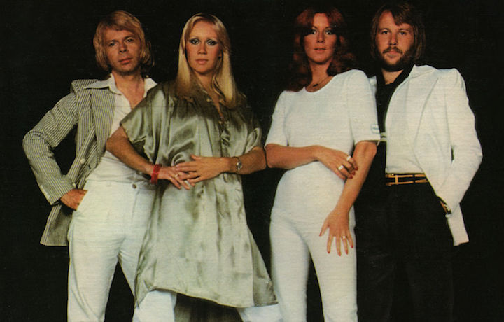Iconic pop group ABBA, poised in stylish 70s attire, exudes the cool confidence of their era, hinting at the timeless music they're celebrated for. Alt Description: Two vibrant pop artists against a surreal desert backdrop, their dynamic poses and colorful attire reflecting the playful and creative spirit of their music collaboration.