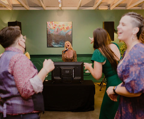 Wedding guests laughing and dancing while singing karaoke together, with a performer leading from the front.