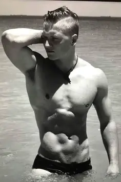 Dave is show in a Sepia image at the beach in black Speedos