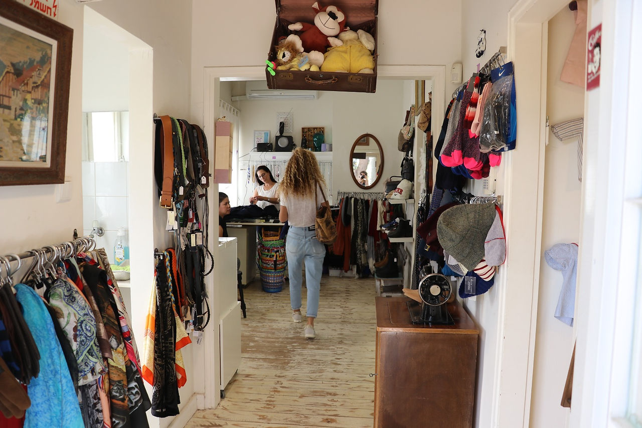 Woman walks through a doorway with various items hanging around, two people inside.