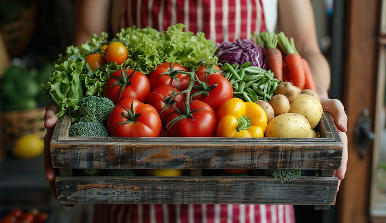 A person holding an open box of fresh vegetables and fruits, including tomatoes, lettuce,