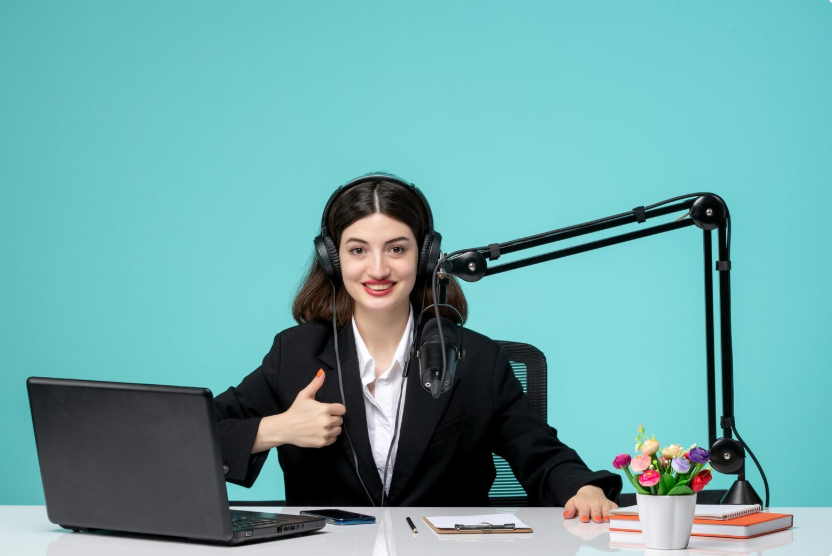White woman with black hair working as a virtual agent at a desk with a microphone and laptop, tailored to meet the hiring company’s needs.