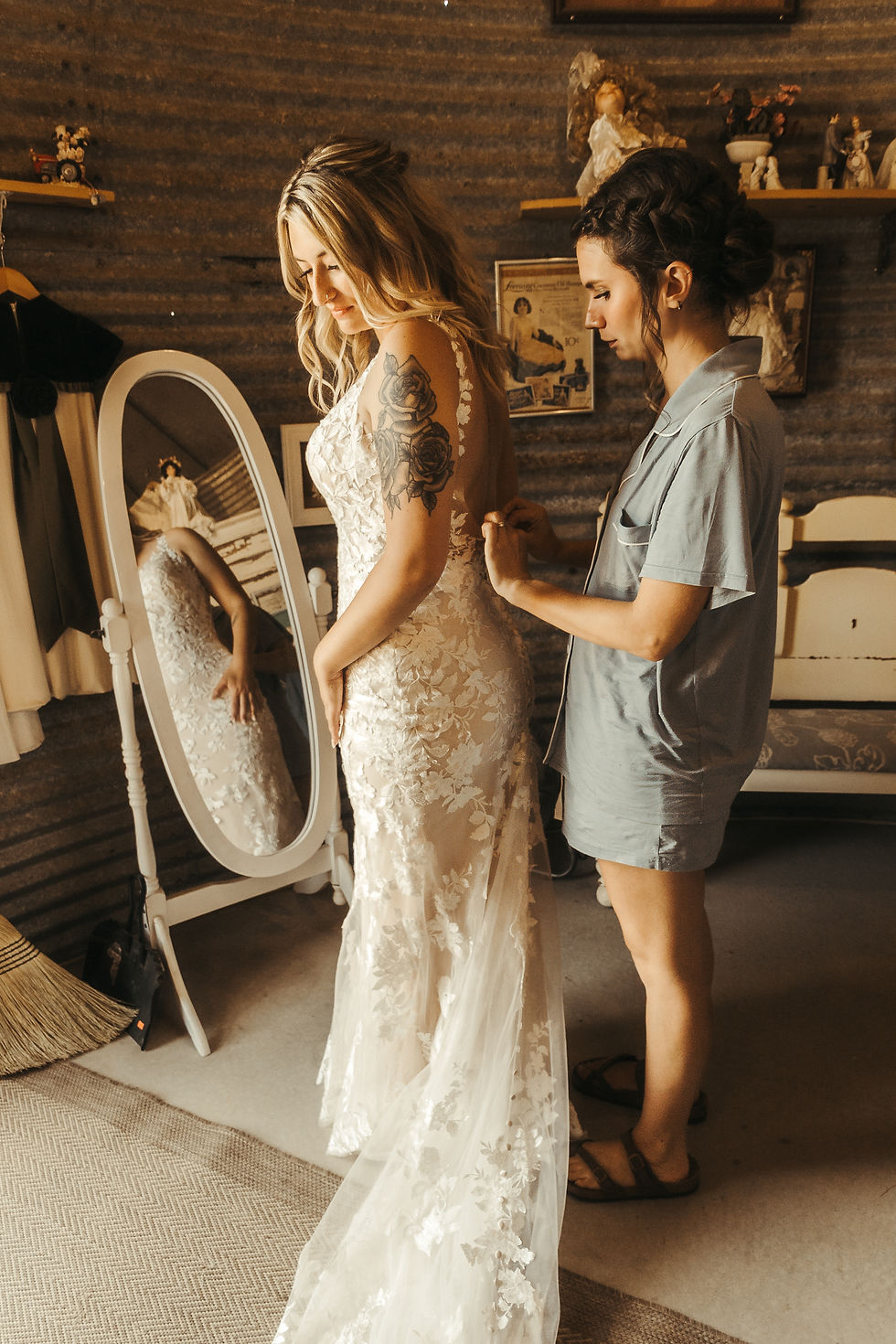 Bridesmaid helping bride into her dress at rustic Minnesota farm venue.