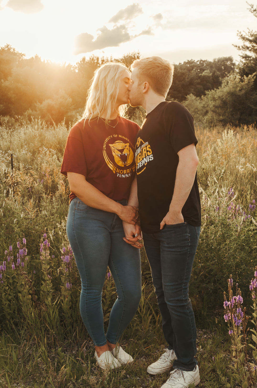 University-themed engagement photo of couple standing in field wearing college gear.