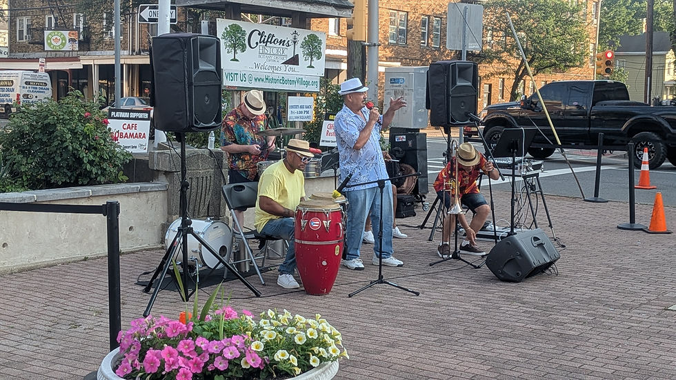 A band performs outdoors with drums and trombone, colorful attire, and speakers. A sign reads "Clifton's Historic Botany District."