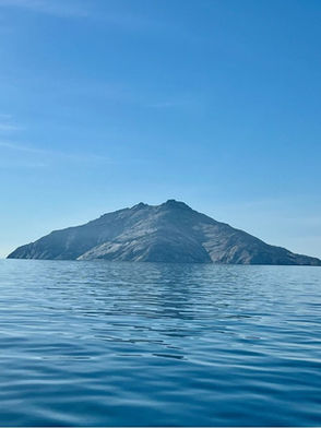 Veduta dell'isola di Montecristo nel Mar Tirreno, ripresa da lontano con cielo sereno e mare calmo