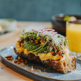 Belegtes Sauerteigbrot mit Ei, Avocado und frischen Kräutern auf einem Teller.