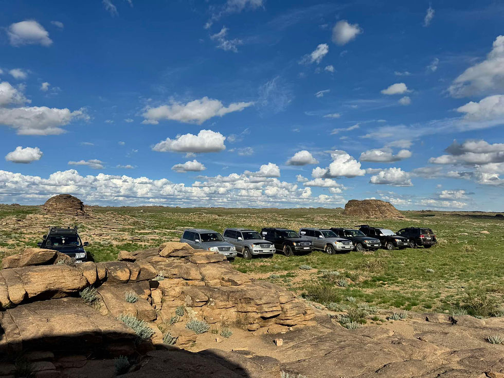 Tour SUVs parked at a viewpoint above wide open plains in Mongolia under a blue sky with clouds