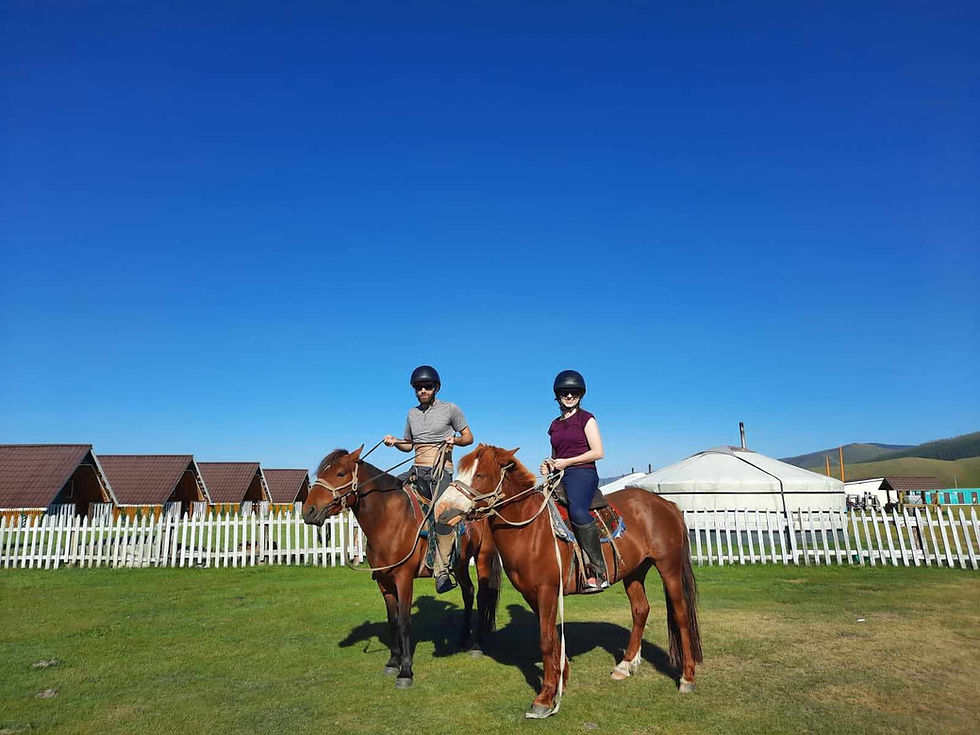 Two riders on horses beside the white fence and gers of a tourist ger camp in the Mongolian countryside