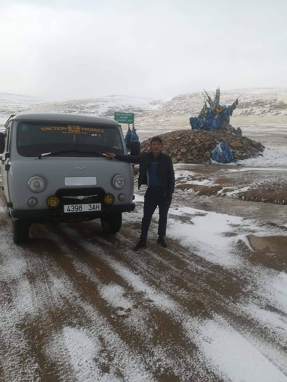 A grey UAZ van on a muddy country track in Mongolia with snow on the ground