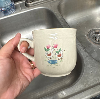 The back of a heartland mug that shows two geese walking with two flowers and water.