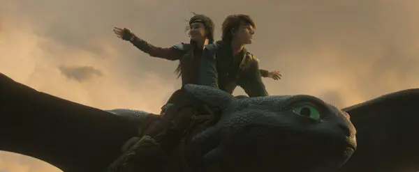 Two characters ride a dragon through a cloudy sky at sunset, arms outstretched. The dragon has large green eyes, setting a mood of adventure.
