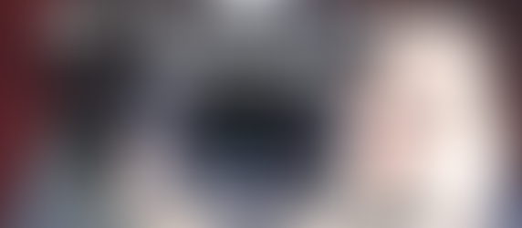 Camera lens held close, text overlaid reads: "How I Fell Back in Love with Photography (And How You Can Too)." Dark background creates focus.