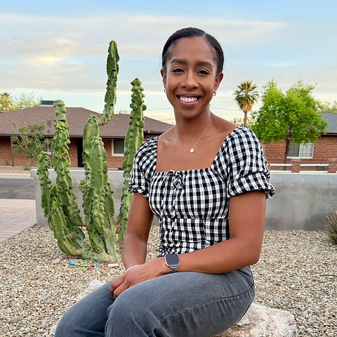 Janet Viloria sits in front of cactuses and desert plants.