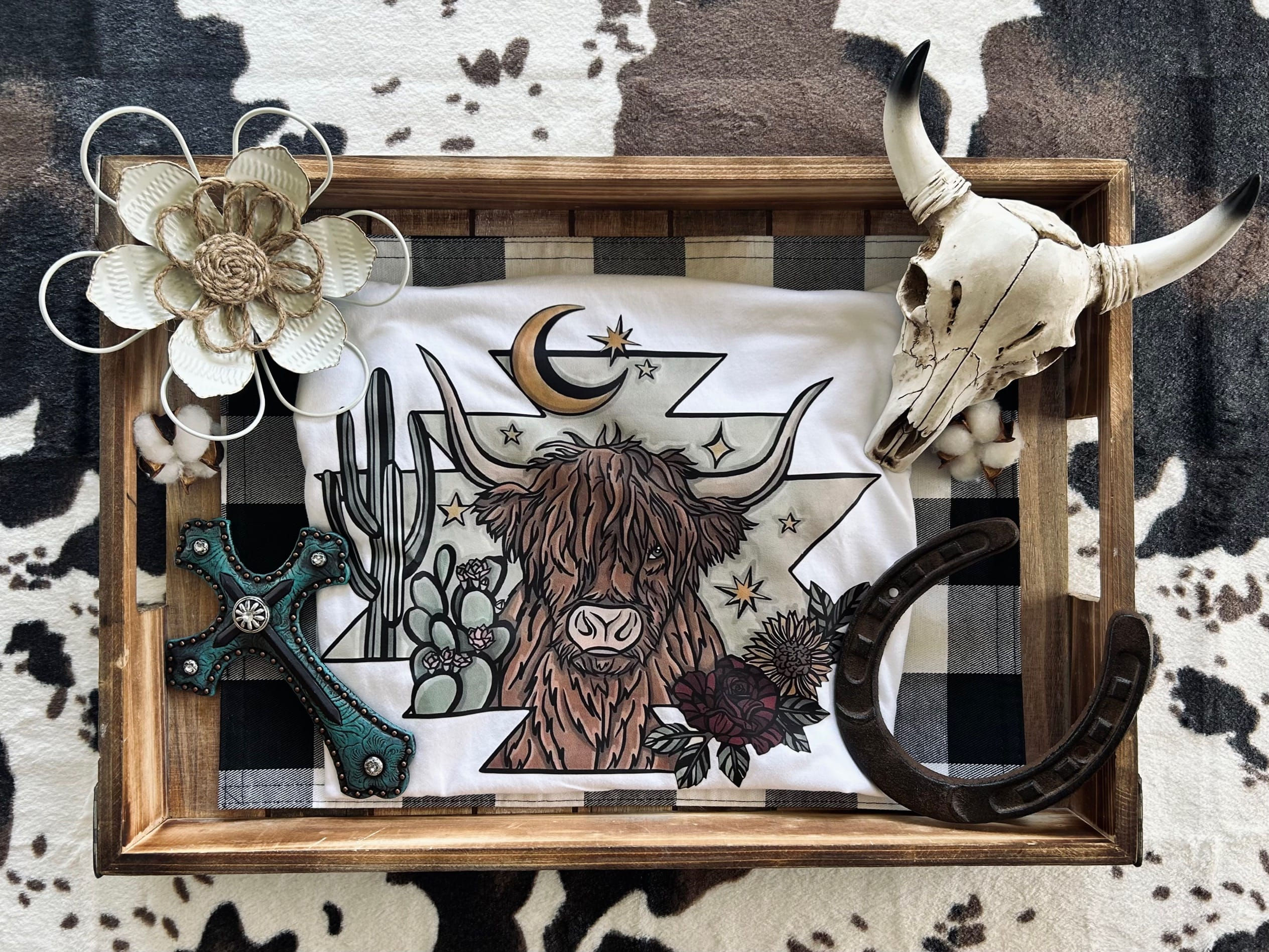 Highland Cow Western Graphic Tee – Features a Highland cow design with plants for country western fashion fans.