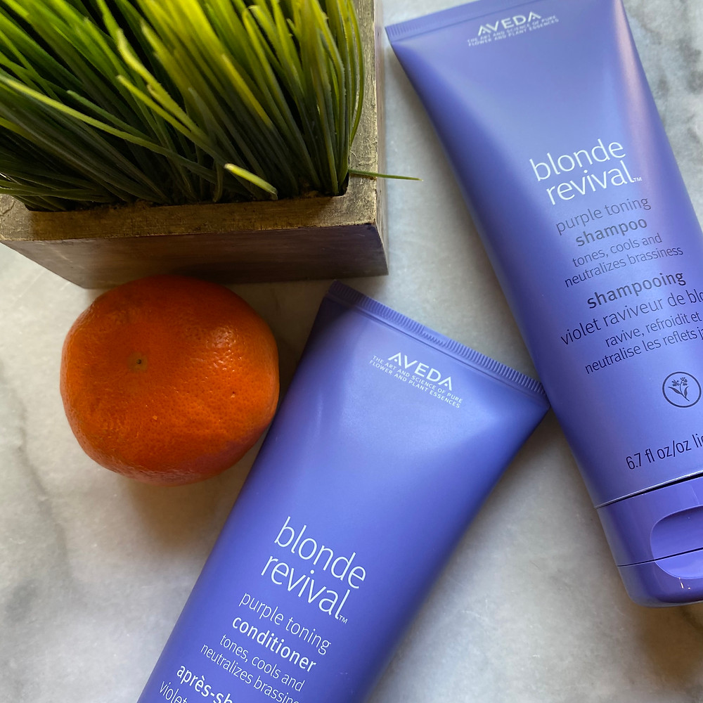 Blonde Revival Purple Toning Shampoo and Conditioner on a marble background with wheat grass and an orange