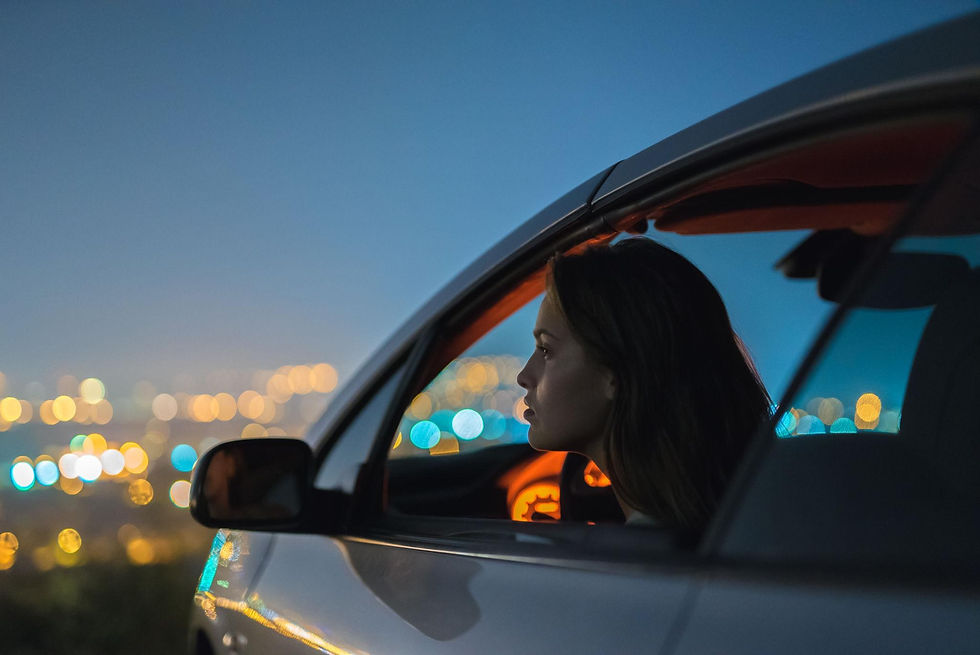 Woman sitting in a car at night looking out the window at city lights.