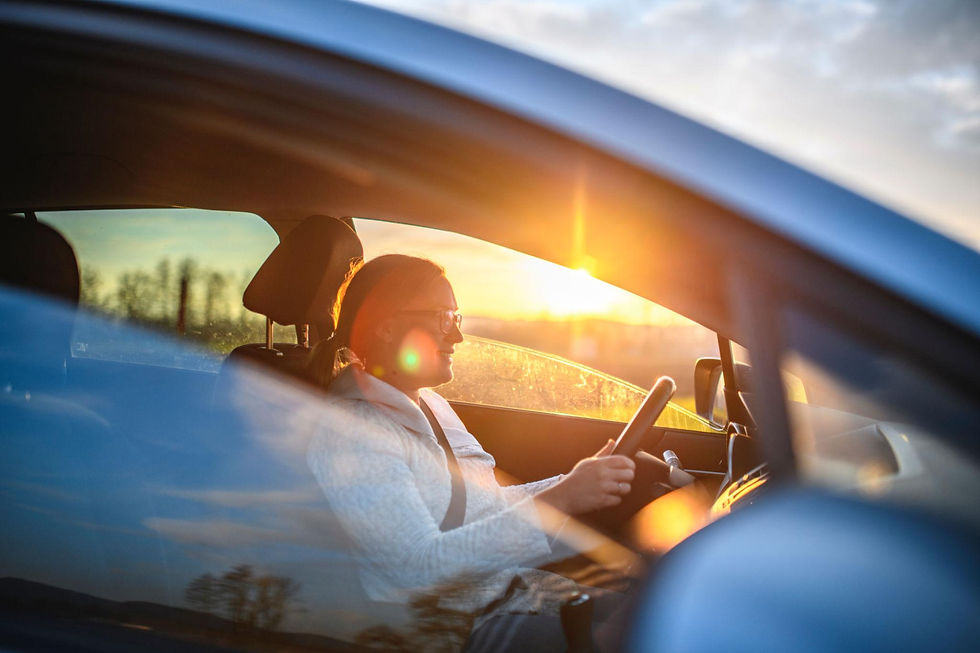 Woman driving a car during sunset with warm sunlight shining through the window.