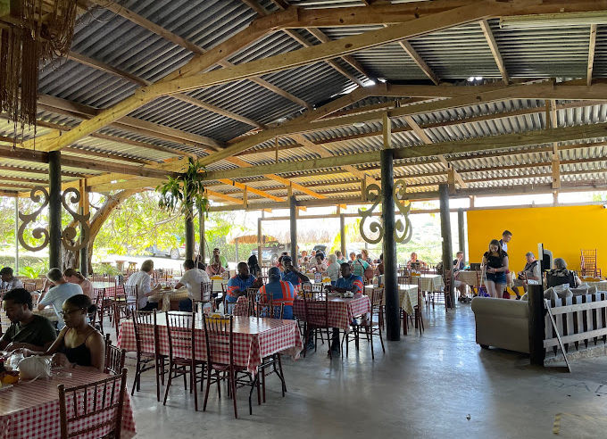 restaurante com mesas com toalha quadriculada espalhadas e pessoas sentadas consumindo e conversando.