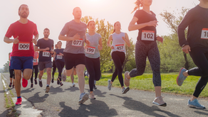 Runners with numbered bibs compete in a marathon on a sunny day, surrounded by greenery and trees, conveying a sense of focus and energy.