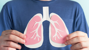 Person in blue shirt holds pink paper lungs cutout against a light blue background, emphasizing respiratory health.