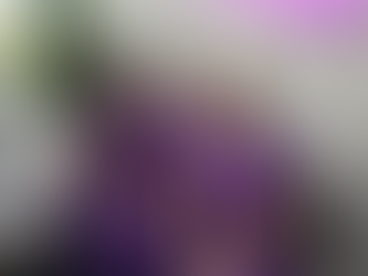 Three women in purple scrubs smile while sitting on a couch inside an office with a leafy plant. A neon sign is partially visible above.