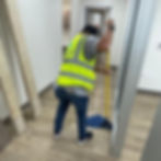 Worker in a yellow vest mopping a wooden floor in a hallway