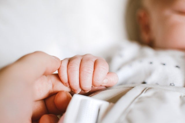 Close up on baby holding parent's finger. Healthy attachment sets the stage for sleep training by boosting your baby's ability to self soothe | The Peaceful Sleeper