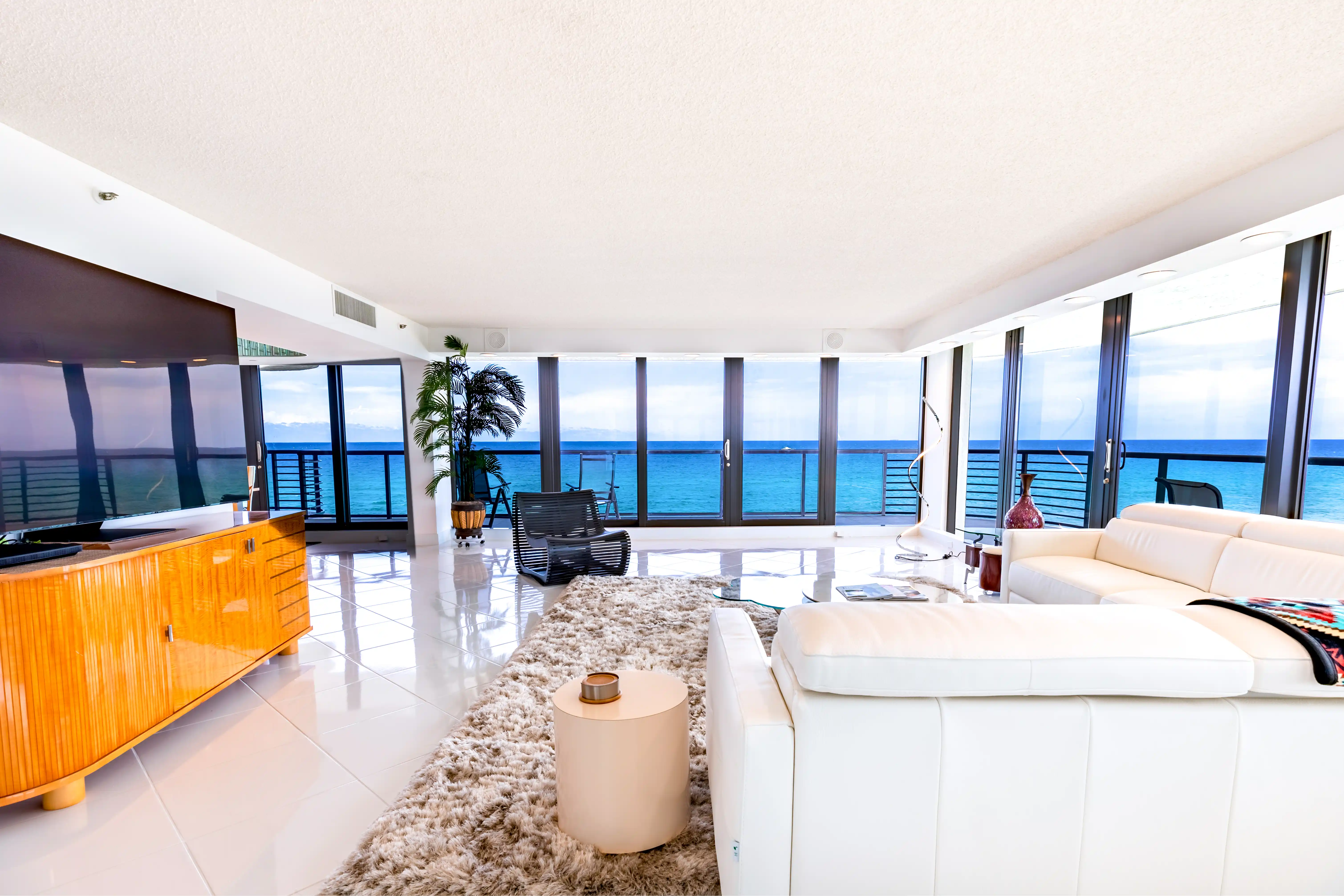 Real estate photography of a modern and bright living room in a Delray Beach condo, The view is of the ocean. The room has floor to ceiling glass windows.
