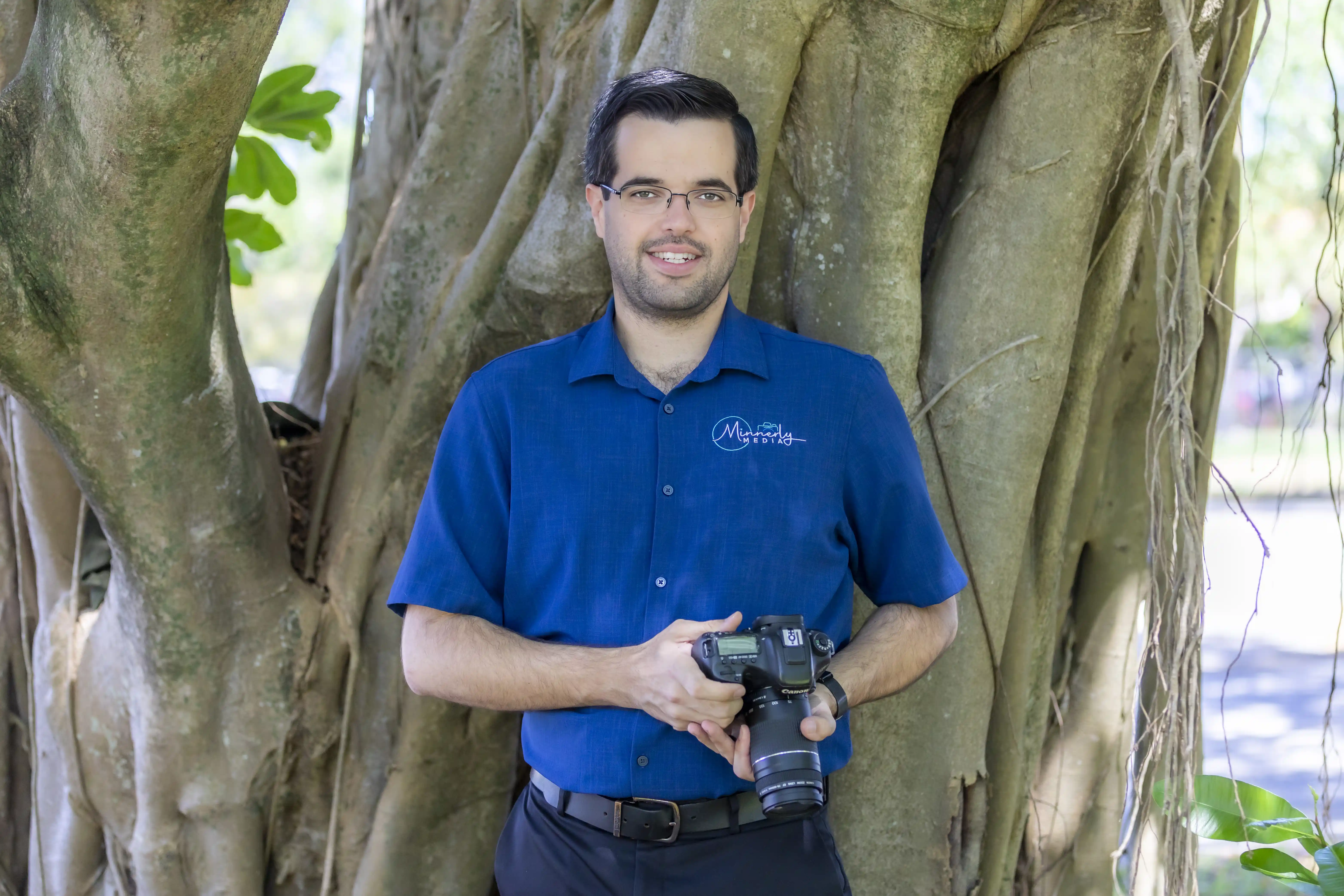 Ian Minnerly, a professional photographer, wearing a blue shirt holding a canon dlsr camera