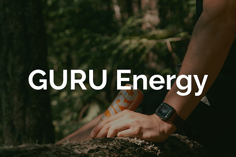 A man's hand holding an orange energy drink in a lush green forest for Lucas Cullen's GURU energy portfolio. 