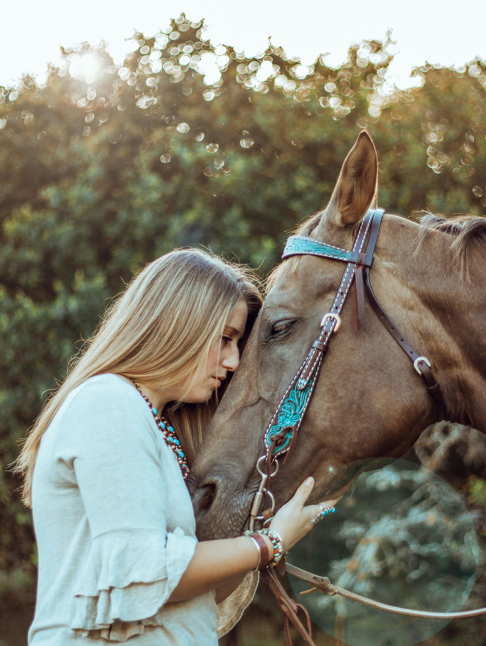 Une femme pose son front contre celui de son cheval, dans une lumière dorée