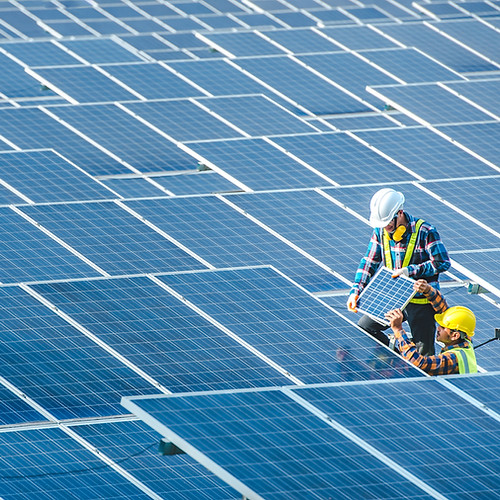 Two construction workers surrounded by solar panels and making repairs