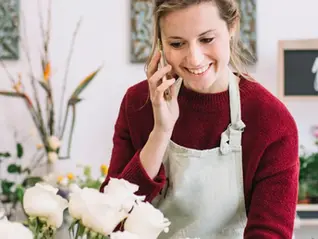 Florist arranging white roses while calling a customer for Mother’s Day flower order in shop