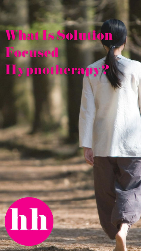 Woman with long black hair, long white shirt, dark trousers and bare feet walking through a sunlit forest path, surrounded by tall trees and greenery, conveying tranquility. Find new pathways